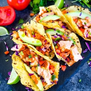 Salmon Tacos recipe on board with cilantro, avocado salsa.