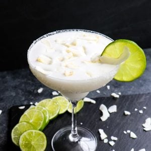 Coconut margarita recipe, with lime slices and coconut flakes.