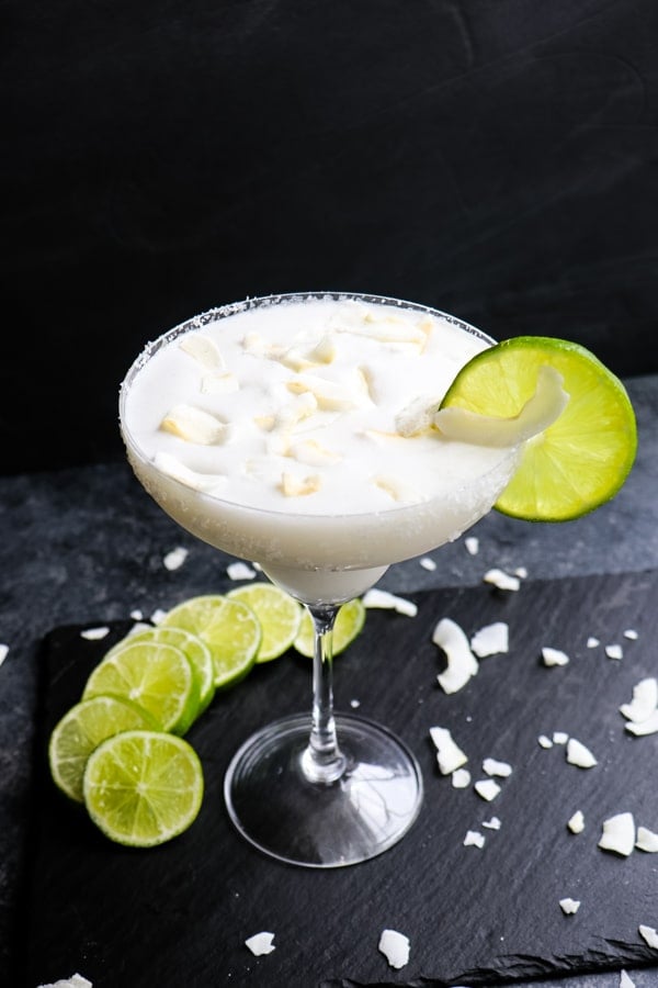 Coconut margarita recipe, with lime slices and coconut flakes.