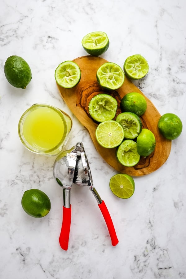 Limes squeezed for lime juice, juice in jar with citrus juicer.