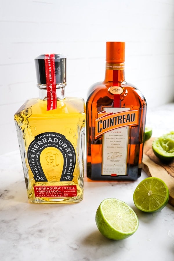 Herradurra tequila and cointreau liqueur bottles with lime halves.