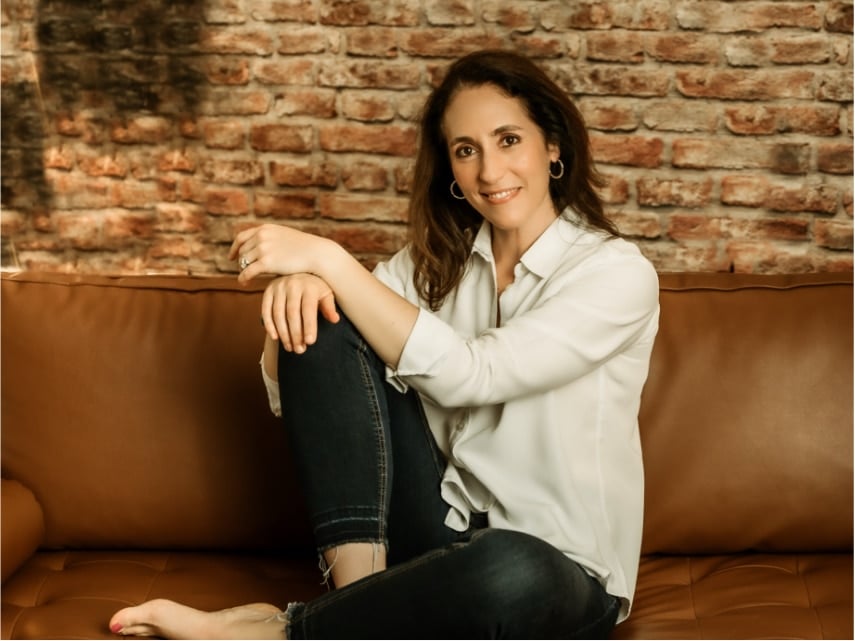 Photo of Erin on leather couch wearing a white shirt and jeans.