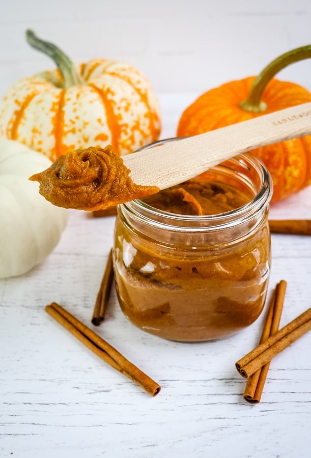 Pumpkin butter in mason jar and on spatula. Garnished with cinnamon sticks and mini pumpkins.