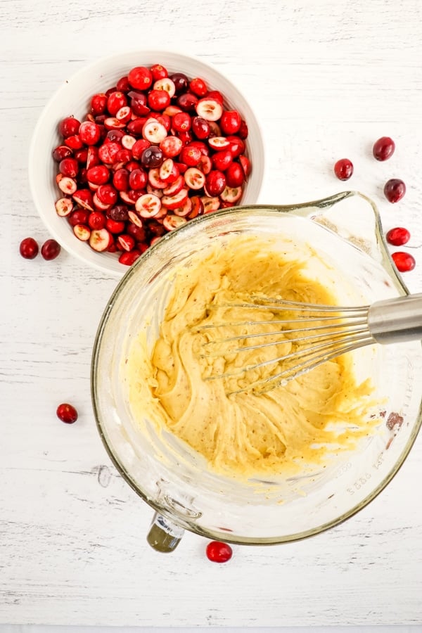 Coffee cake batter mixed with a whisk, cranberries on the side.