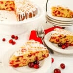 Slices of cranberry coffee cake on plates with whole cake on cake plate.