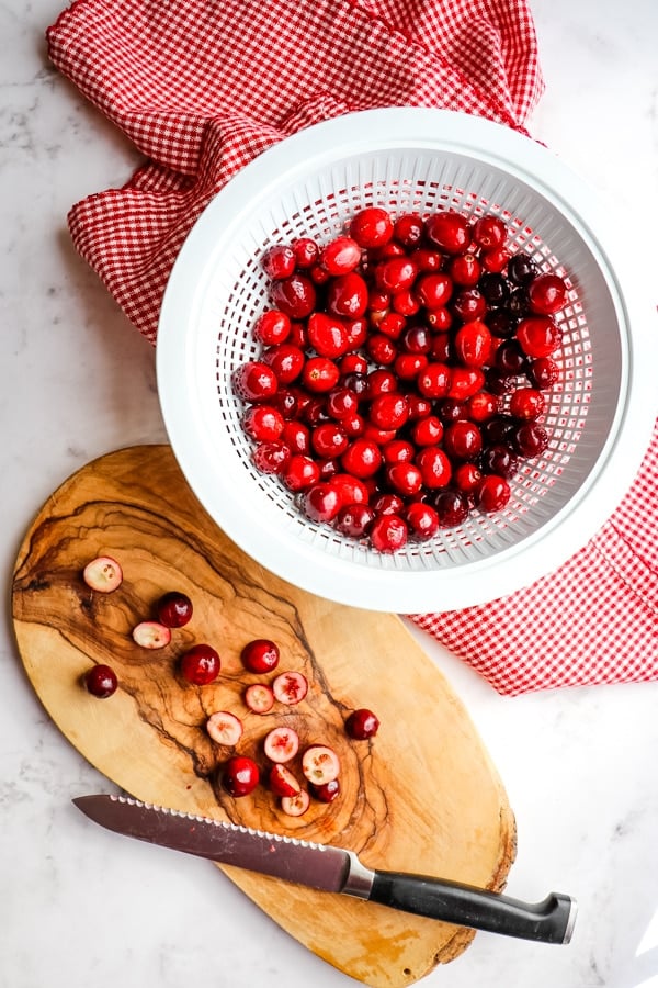 Colander with rinsed cranberries and berries cut on a cutting board with knife.