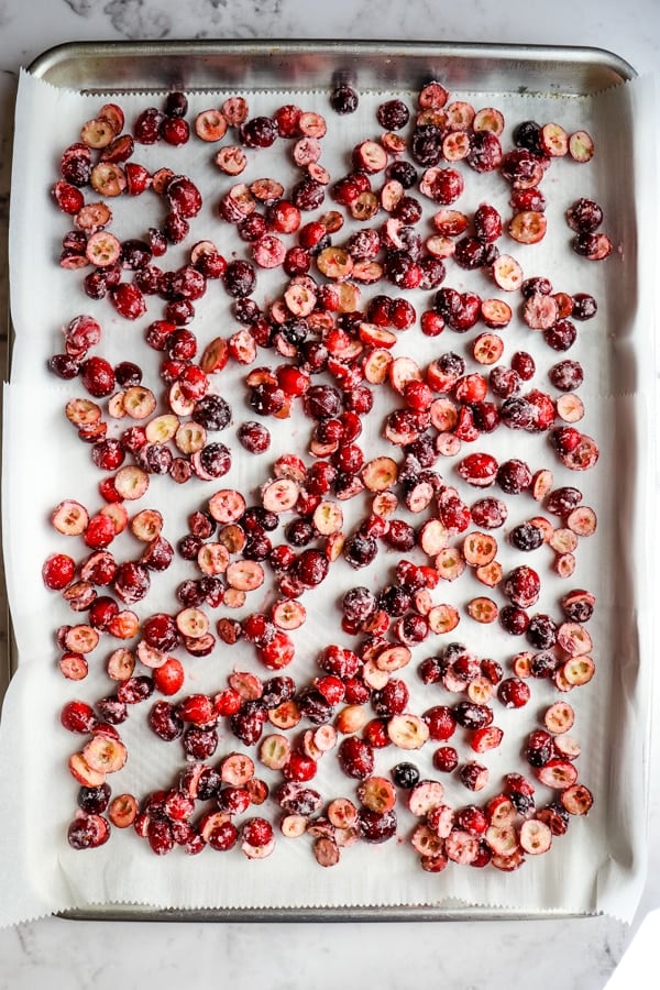 Sheet pan with coated cranberries on parchment paper.