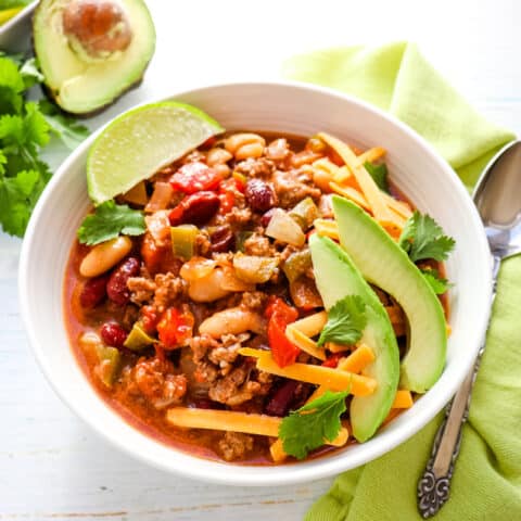 Bowl of crock pot chili topped with cheese, cilantro, avocados and lime wedge.