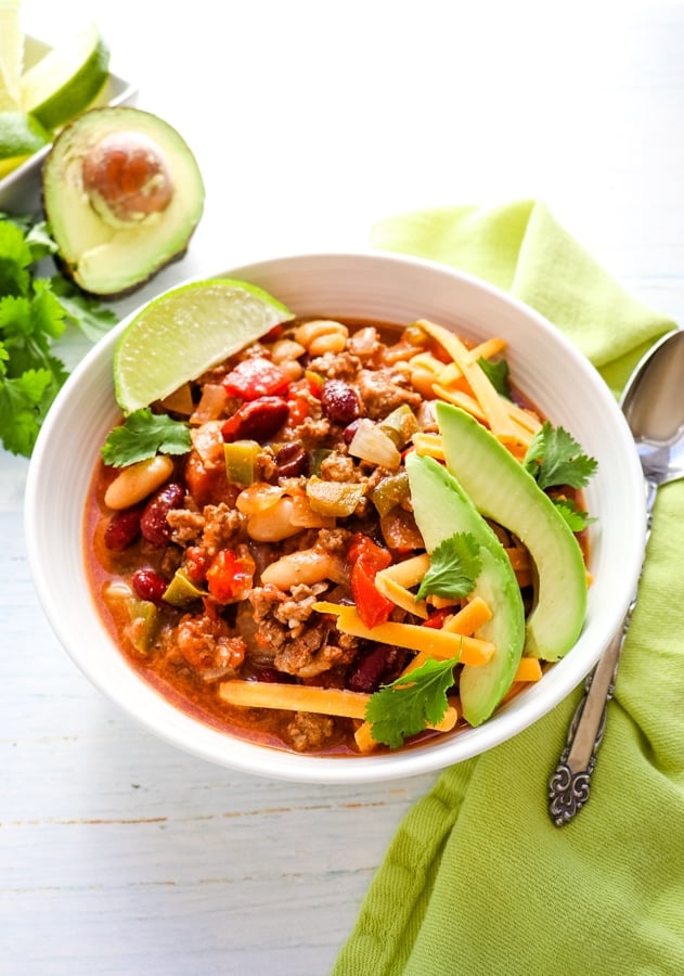 Bowl of crock pot chili topped with cheese, cilantro, avocados and lime wedge.