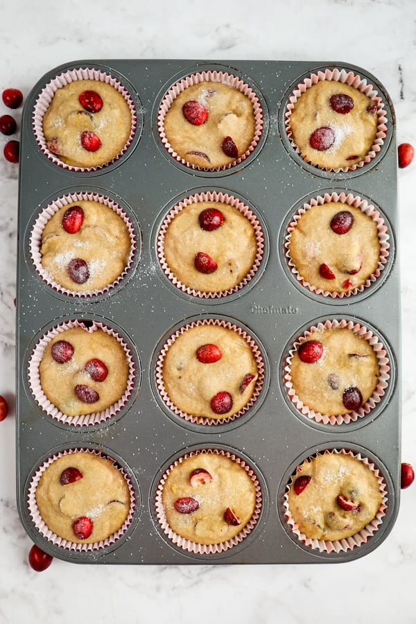 Cranberry orange muffin batter poured into muffin tin and topped with fresh cranberries.