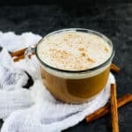 Mug of eggnog latte topped with nutmeg and garnished with cinnamon sticks.