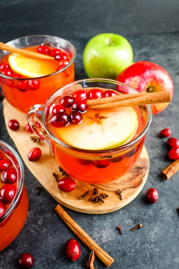 Mug of hot mulled apple cider topped with cranberries, apple slice and cinnamon stick.
