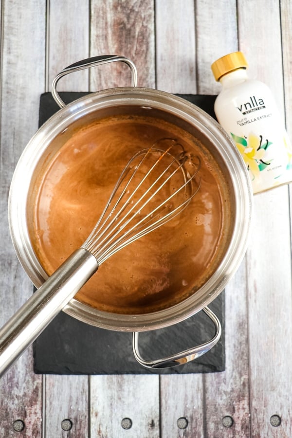 Whisking together hot chocolate in saucepan with vanilla on the side.