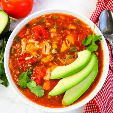Bowl of chicken enchilada soup topped with avocados and cilantro.