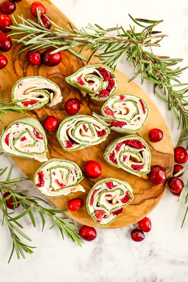 Cranberry turkey roll ups on board, garnished with cranberries and rosemary.