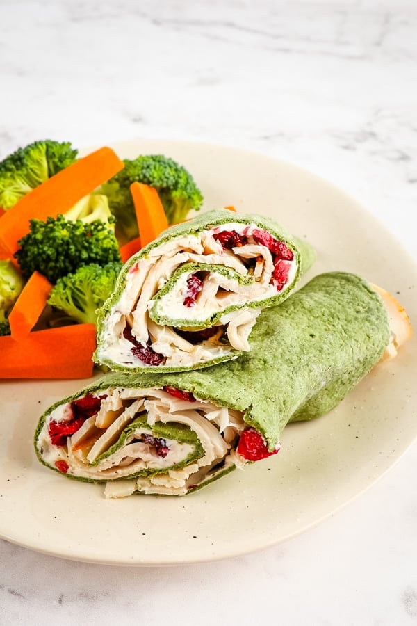Healthy turkey wrap on plate with fresh vegetables.