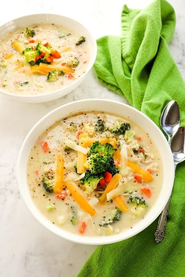 Two bowls of healthy chicken broccoli cheese soup with green napkin and spoons on the side.
