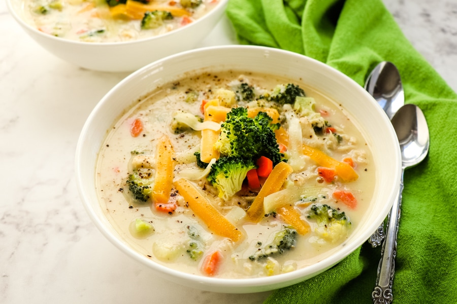 Bowl of healthy chicken broccoli cheese soup, with green napkin and spoons on the side.
