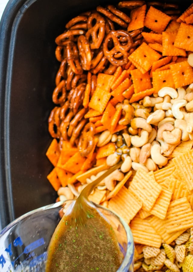 Sauce being poured over snack mix in slow cooker.