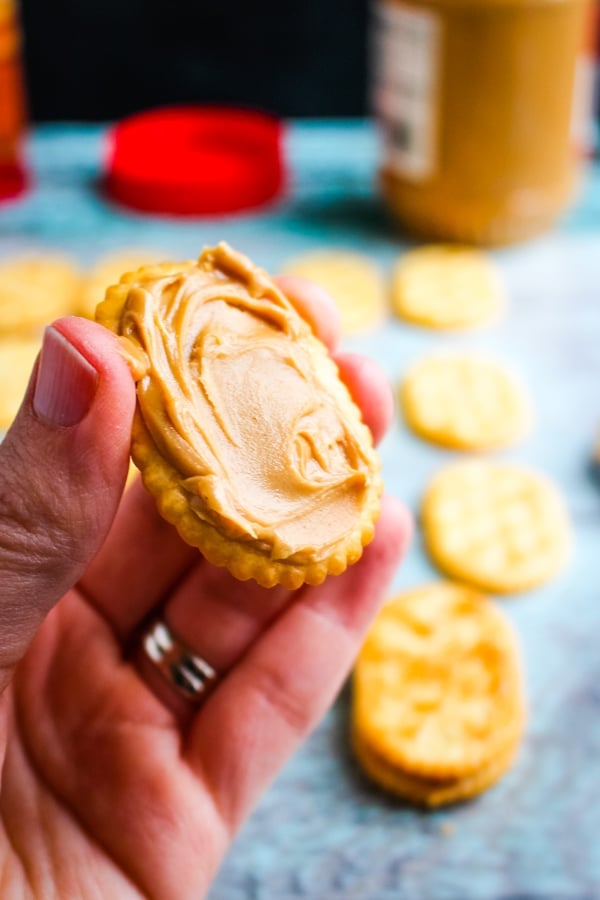 Creamy peanut butter spread on to cracker for penguin cookies.