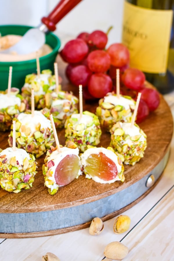 Pistachio grape cheese appetizers on serving board with grapes and wine.