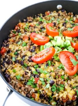 Healthy easy taco casserole in skillet topped with tomatoes and avocados.