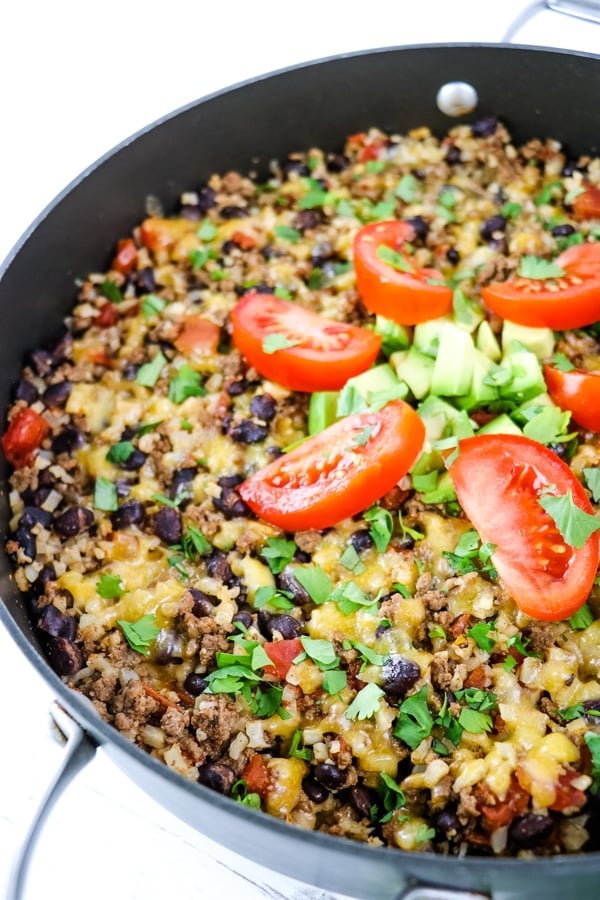 Mexican beef in skillet topped with tomatoes, cilantro and avocados.