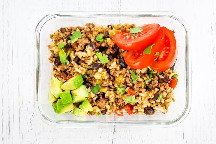 Meal prep container with healthy taco casserole topped with tomatoes and avocados.