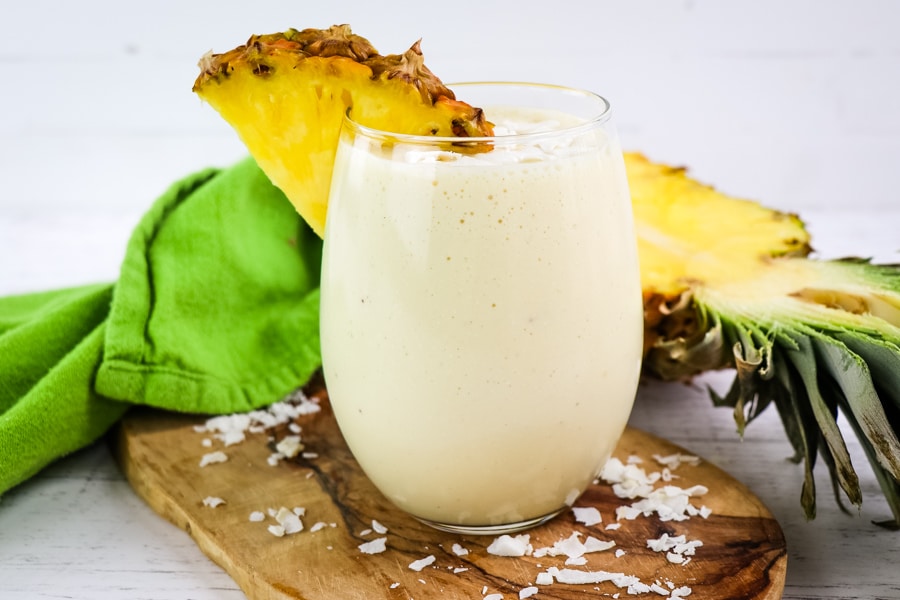 Pina colada smoothie garnished with pineapple slice and coconut flakes.