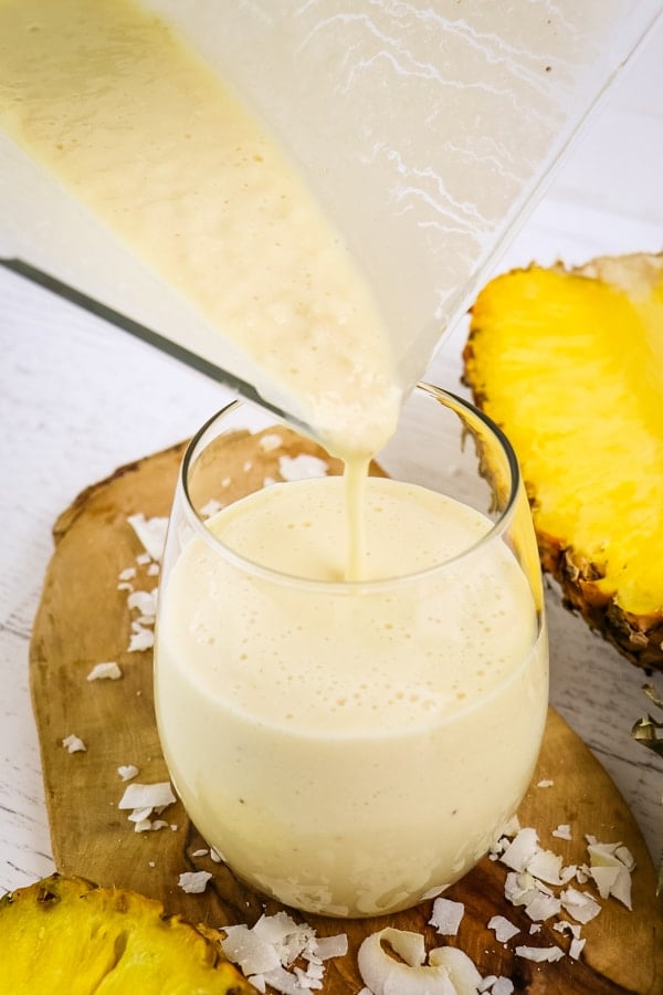 Pouring pina colada smoothie into glass from blender jar.