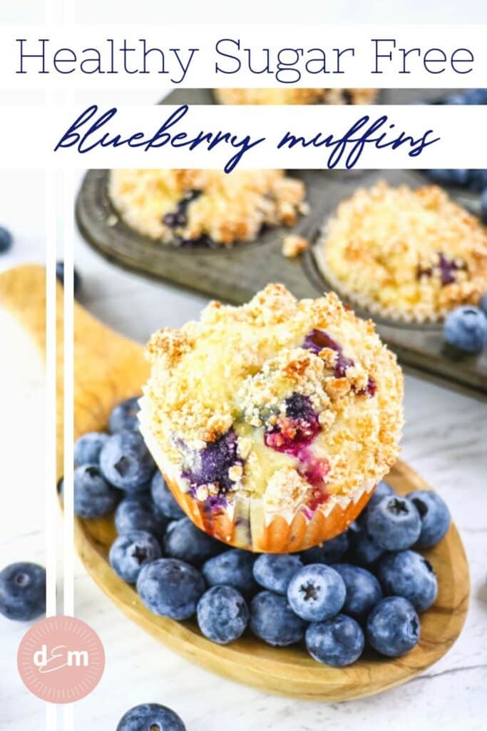 Healthy blueberry muffin sitting on top of fresh blueberries, with more muffins in background.