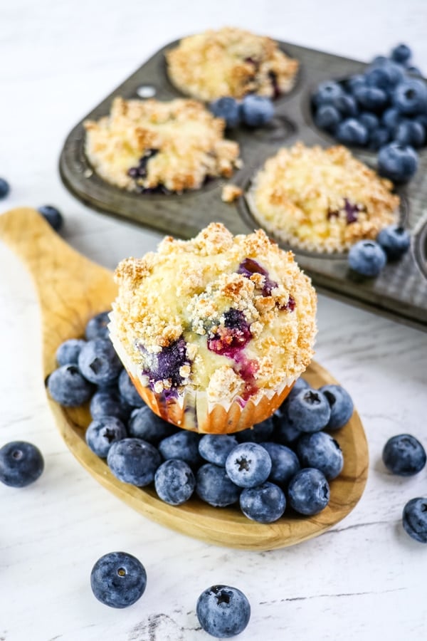 Healthy blueberry muffin sitting on top of fresh blueberries, with muffins in tin in the background.