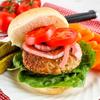 Turkey burger, on plate, topped with onions, tomatoes and pickles and carrots on the side.