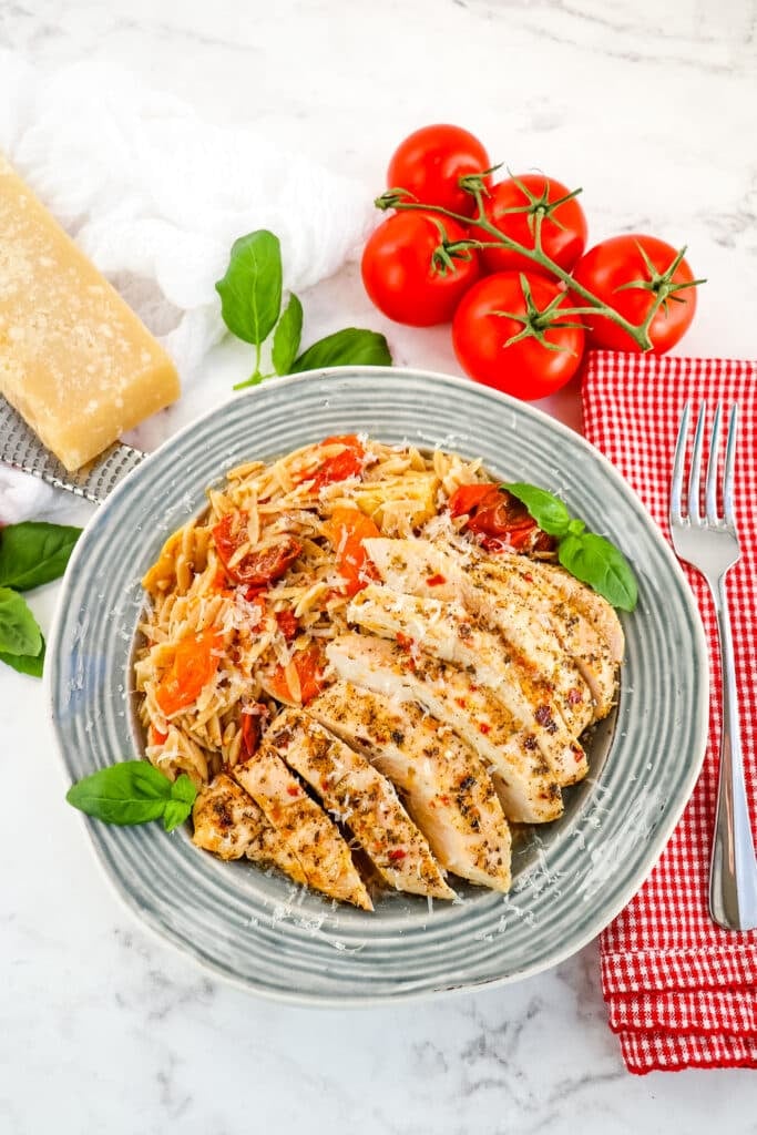 Baked Italian chicken with tomato orzo on the side and topped with grated mozzarella cheese.