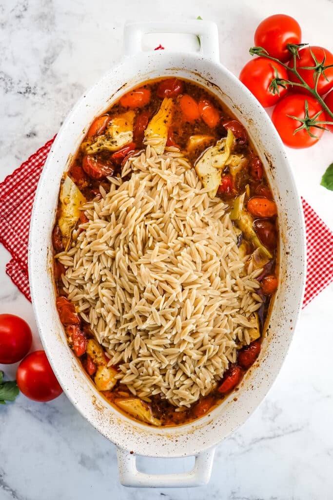 Whole wheat orzo pasta in baking dish with baked cherry tomatoes and artichokes.