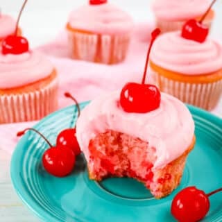 Cherry cupcake on blue plate, garnished with maraschino cherries, with bite taken out of cupcake.