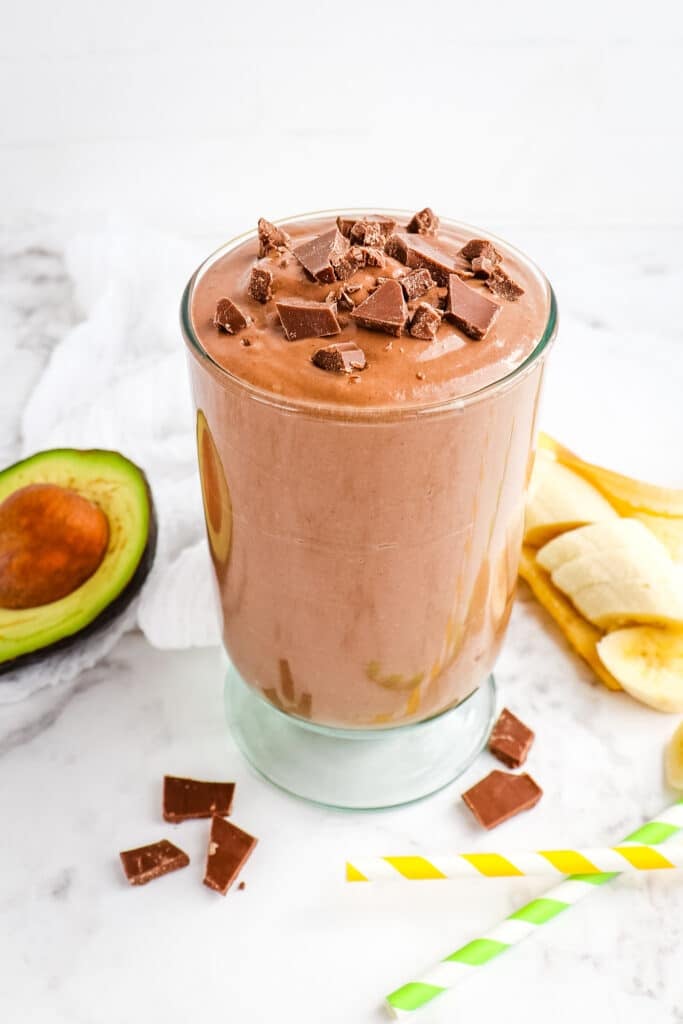 Chocolate avocado smoothie, in glass, topped with chocolate chunks.