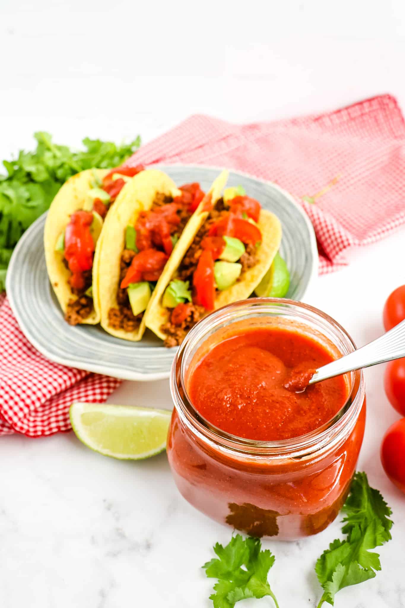 Homemade taco sauce in jar, with plate of tacos in background.