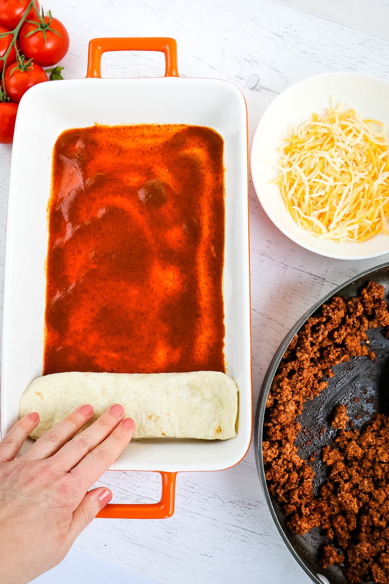 Rolled enchilada being placed in pan with enchilada sauce.