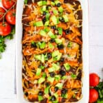 Red sauce been enchiladas that have been topped with avocados, olives and tomatoes.