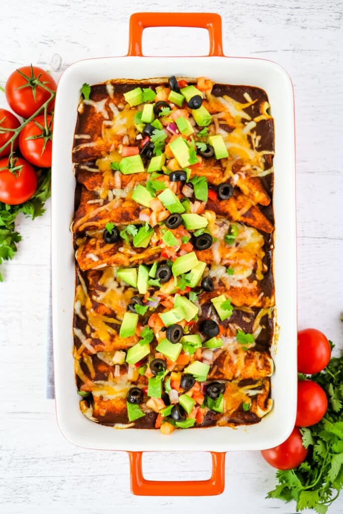 Red sauce been enchiladas that have been topped with avocados, olives and tomatoes.