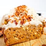 Slice of frosted healthy carrot cake loaf, topped with pecans and carrot shreds.