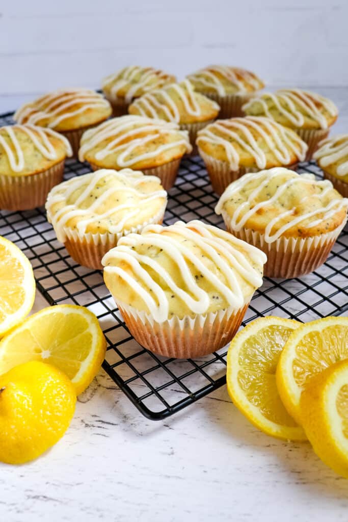 Glazed lemon poppy seed muffins on cooling rack with lemon slices.