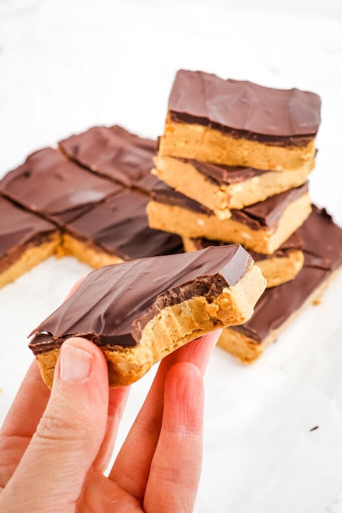 Peanut butter protein bars in a snack and held in hand with bite.