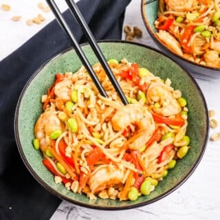 Shrimp stir fry with noodles and vegetables in bowl with chop sticks.