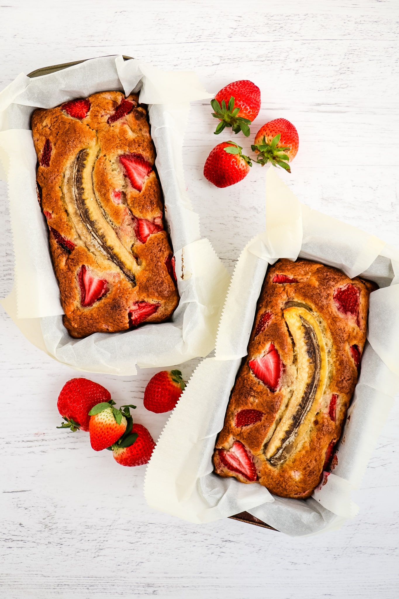 Two loaves of baked strawberry banana bread still in loaf pans.