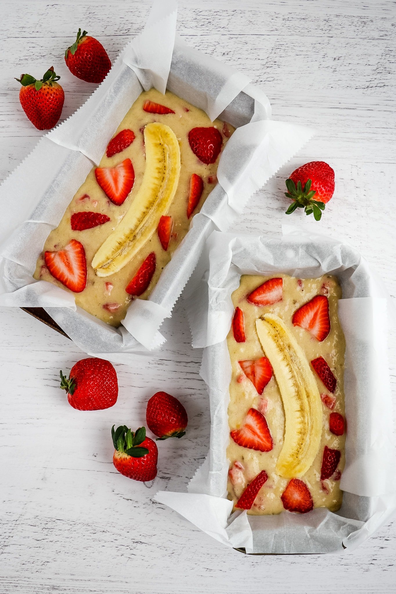 Strawberry banana bread batter poured into loaf pans and topped with sliced strawberries and halved bananas.