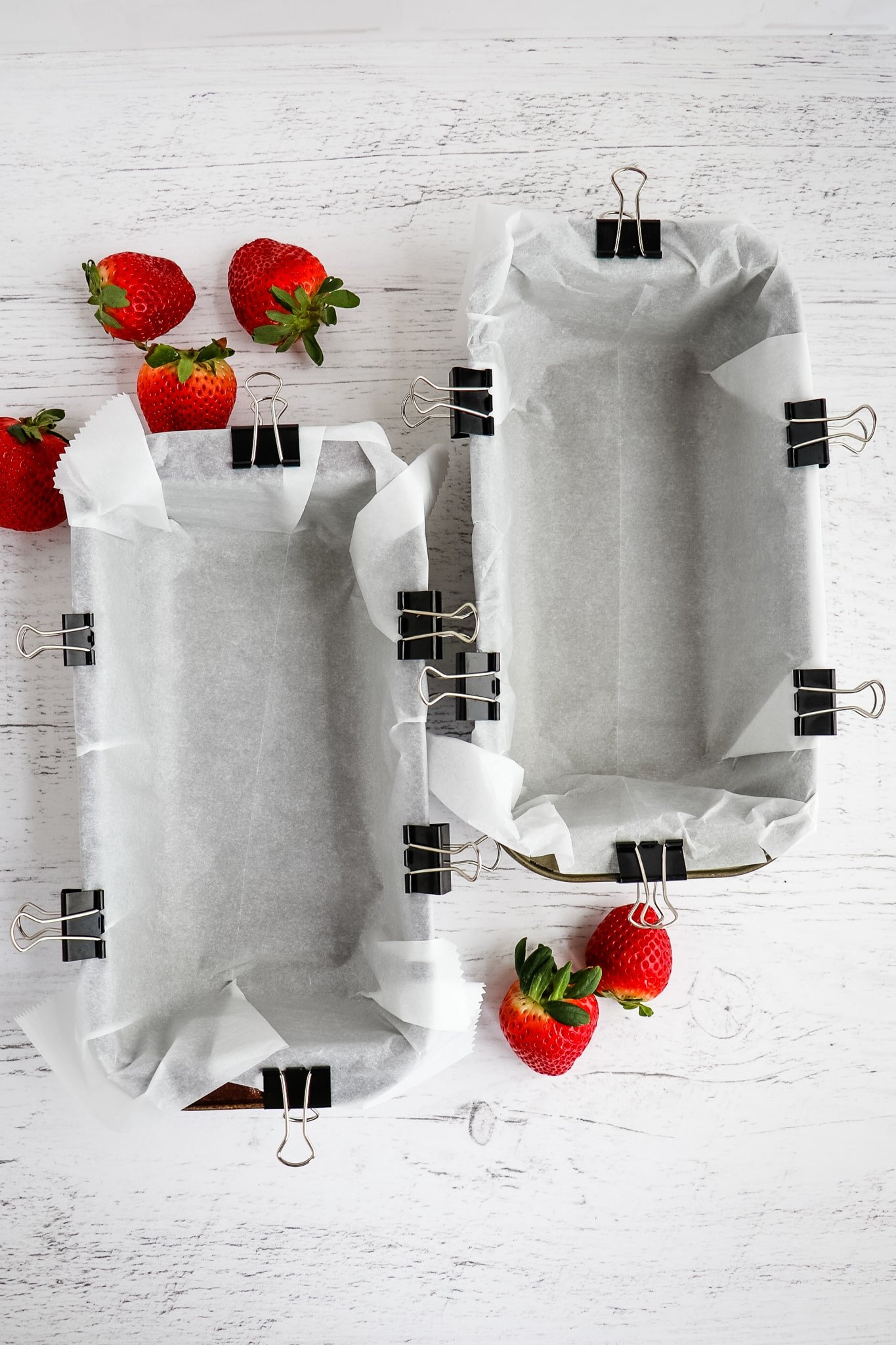 Two loaf pans, lined with parchment paper and secured with binder clips.