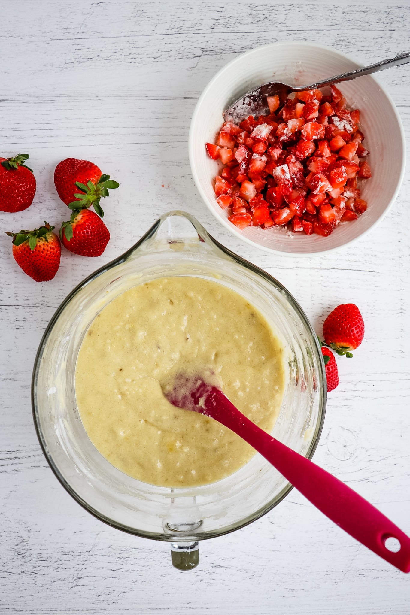 Bowls of banana bread batter and diced strawberries for strawberry banana bread.