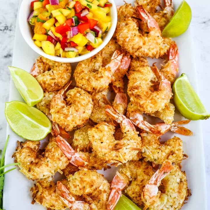 Air fryer coconut shrimp on platter with lime wedges and salsa on the side.